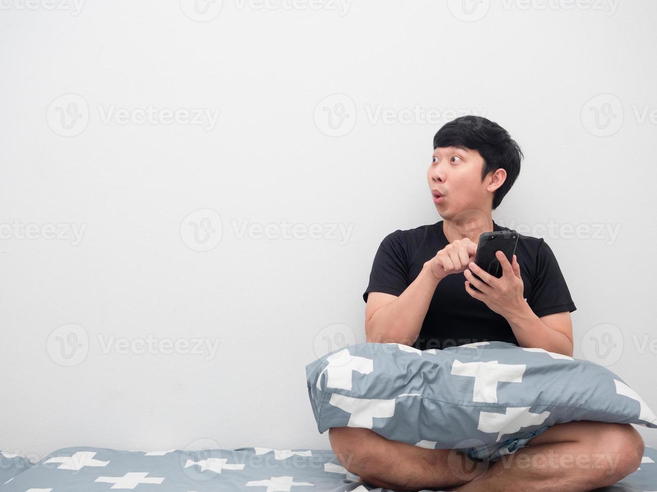 Man using mobile on the bed feeling excited looking at copy space photo