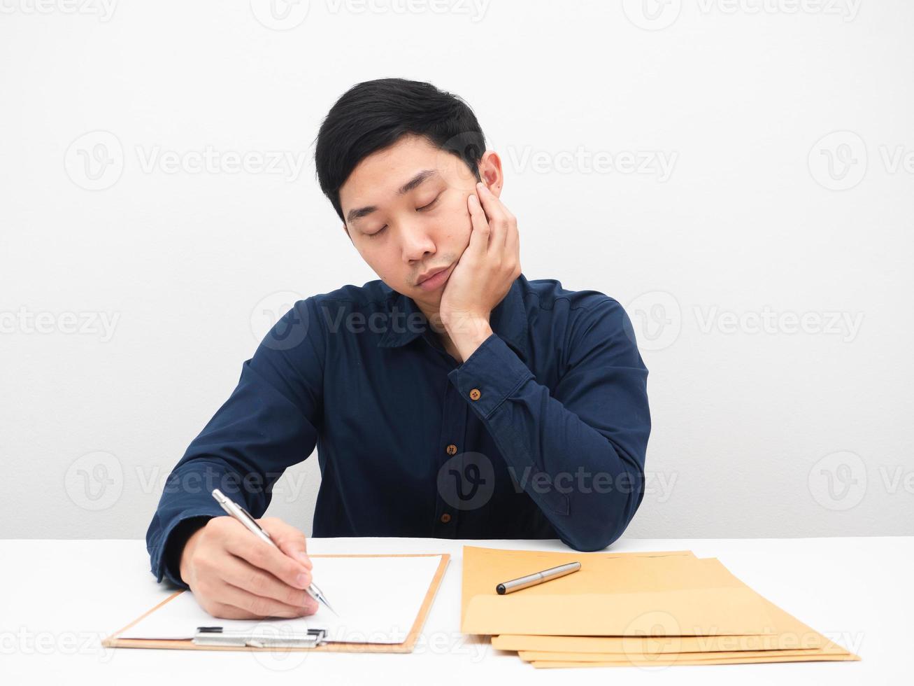 Man writing on paper untill sleep at the table,Man working at his workplace feeling sleepy photo