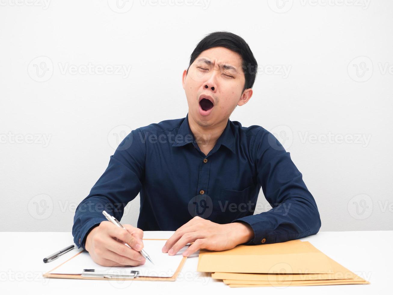 Asian man feeling sleepy and yawn lazy to working at his workplace on table photo