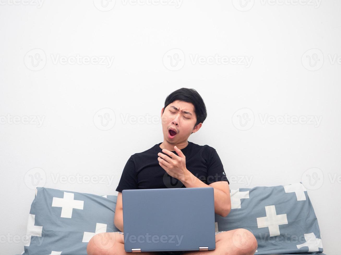 Asian man with laptop sitting on the bed feeling sleepy photo