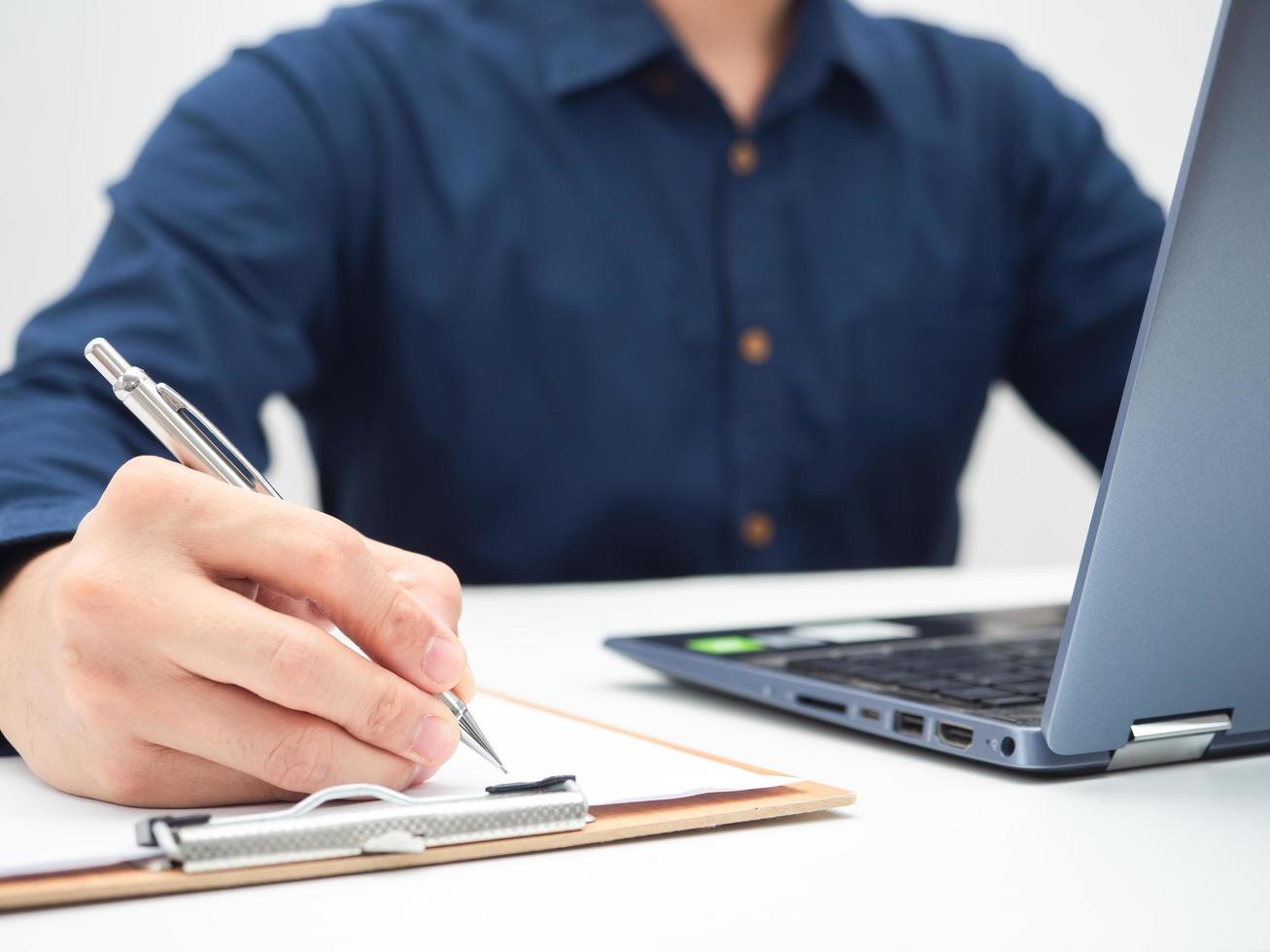 Close up hand of man writing on document board on the table with laptop,Work from home concept photo