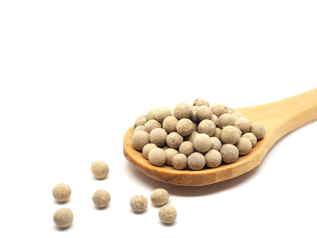 Closeup white peppers in wood spoon on white isolated natural shadow copy space ingredients kitchen concept photo