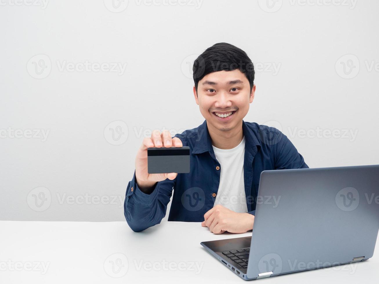 hombre feliz emoción sonriendo sosteniendo tarjeta de crédito y sentarse en el escritorio con la computadora portátil foto