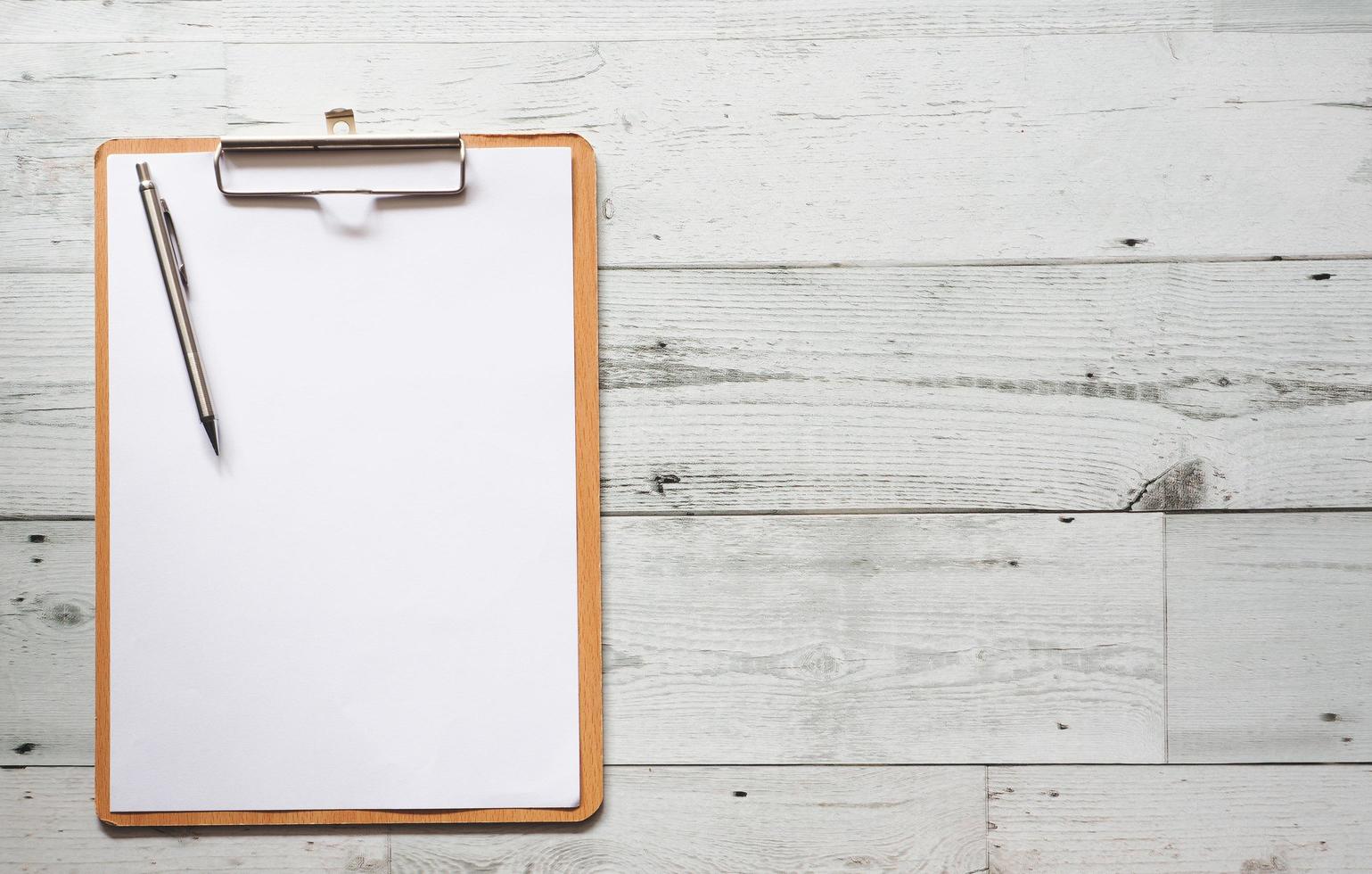 Silver pen on blank white document sheet on wood clipboard on white wood table top view space photo