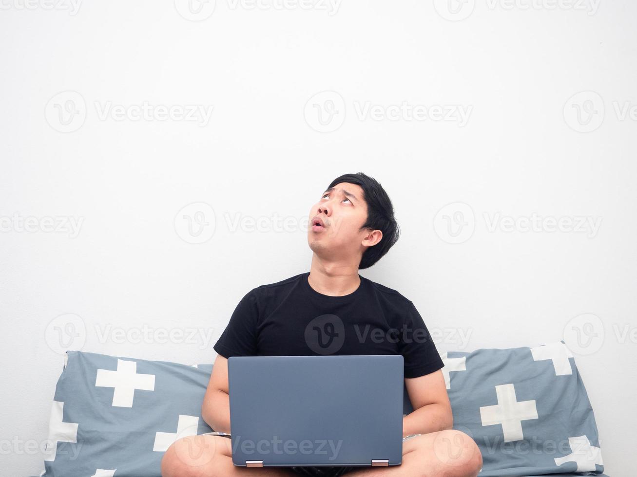 Man with laptop sitting in the bedroom looking up at copy space photo