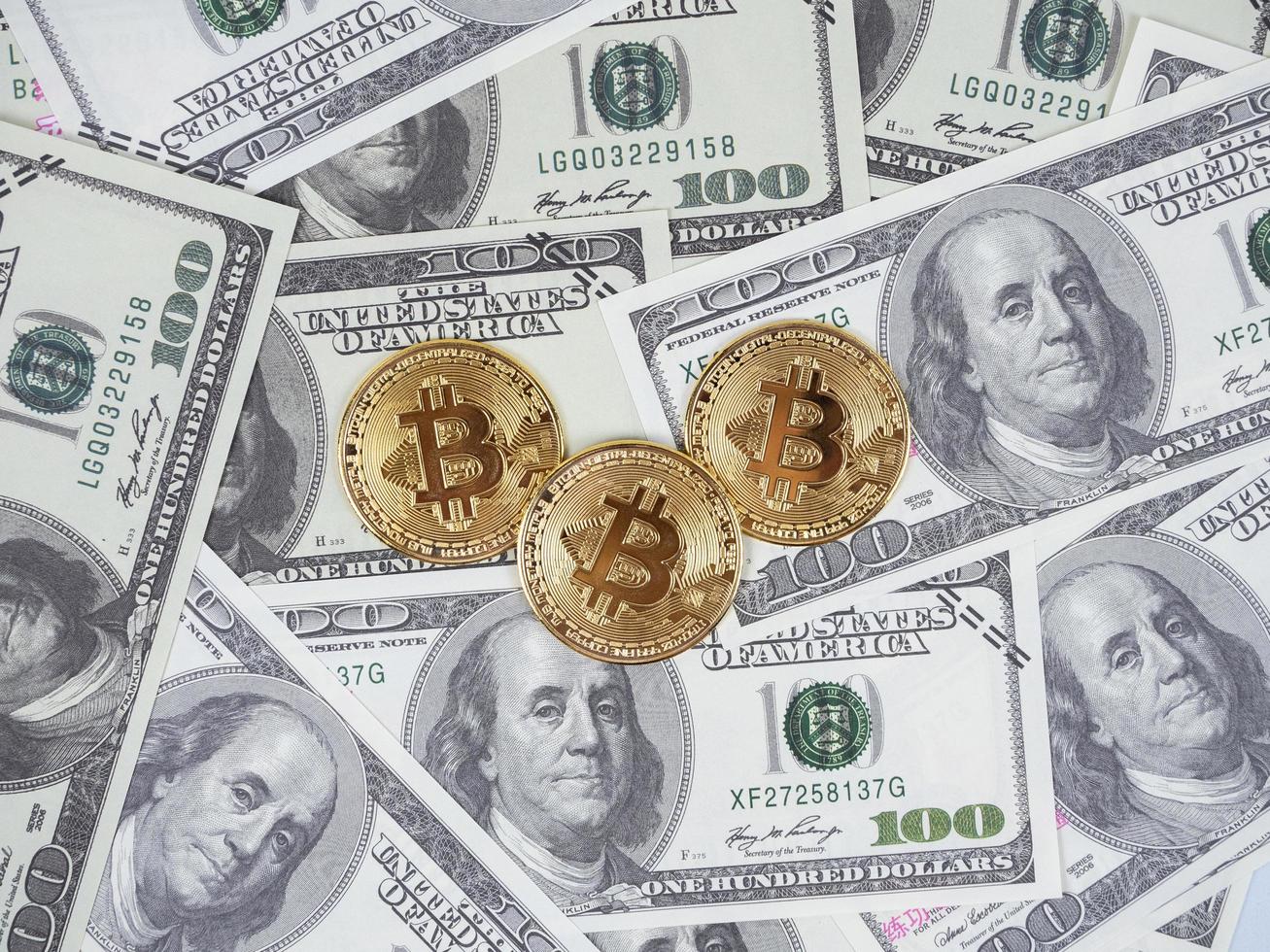 tres bitcoins dorados en una gran cantidad de billetes de dinero vista superior en dólares, concepto de dinero digital foto