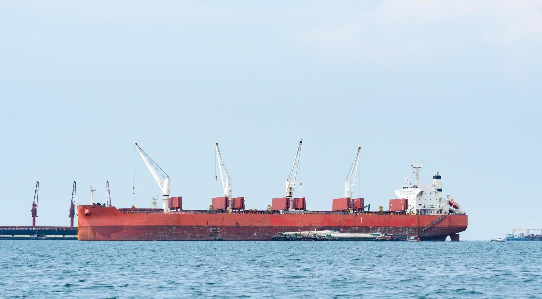 barco grande de color rojo con una gran grúa en el océano azul y el paisaje del cielo azul, barco industrial en el concepto logístico del mar foto