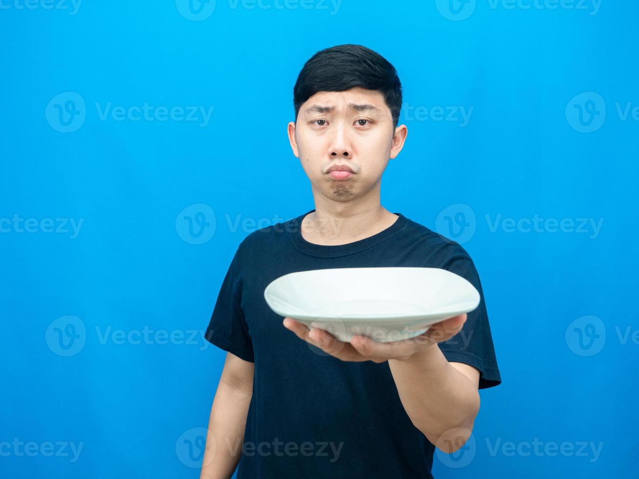 Hungry man holding empty dish gesture want food blue background photo