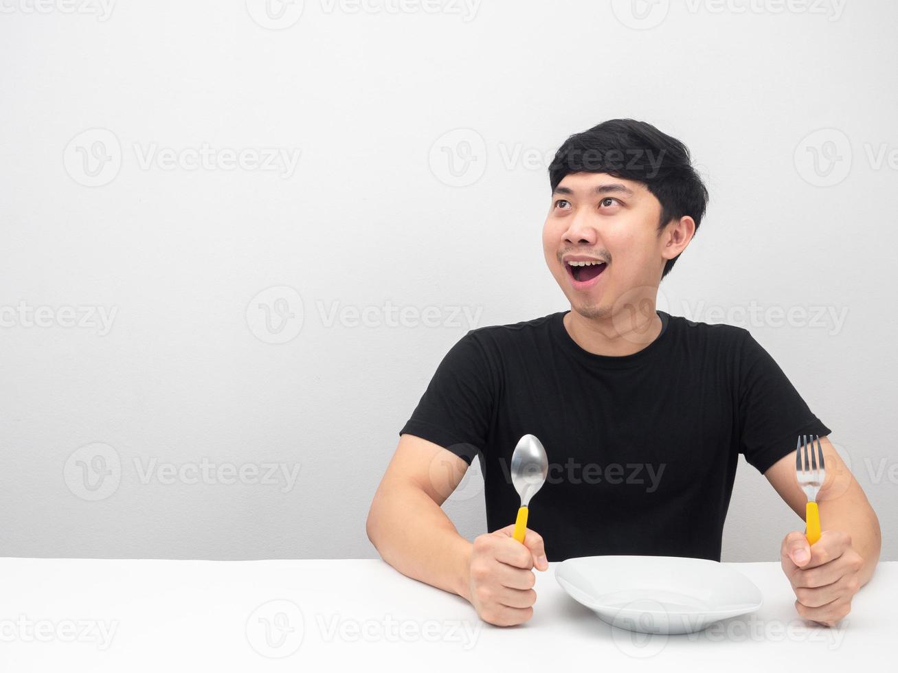 Man holding cutlery sit at the table feeling hungry and looking at copy space photo