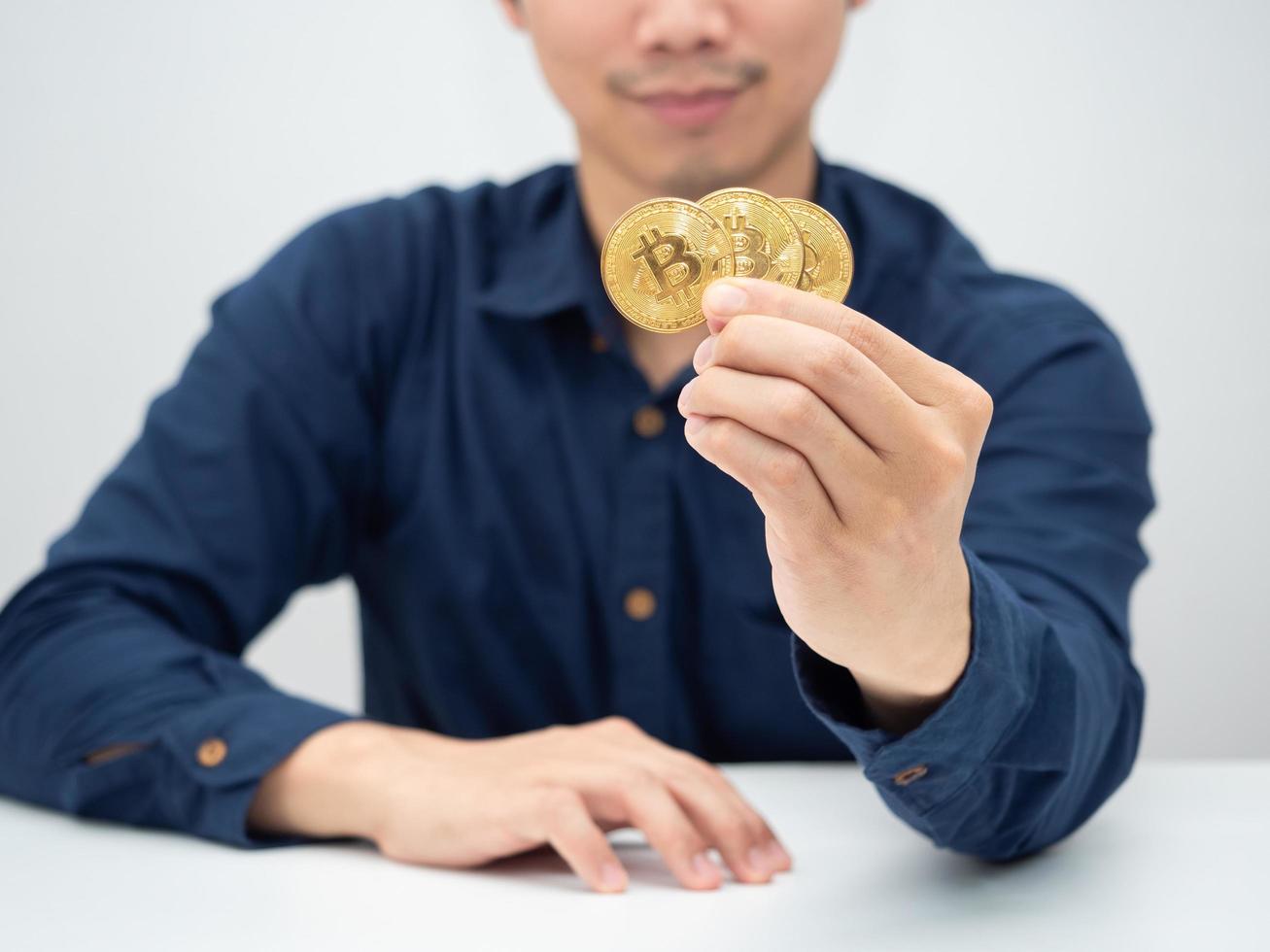 hombre sentado en el escritorio y mostrando bitcoin dorado en su mano foto