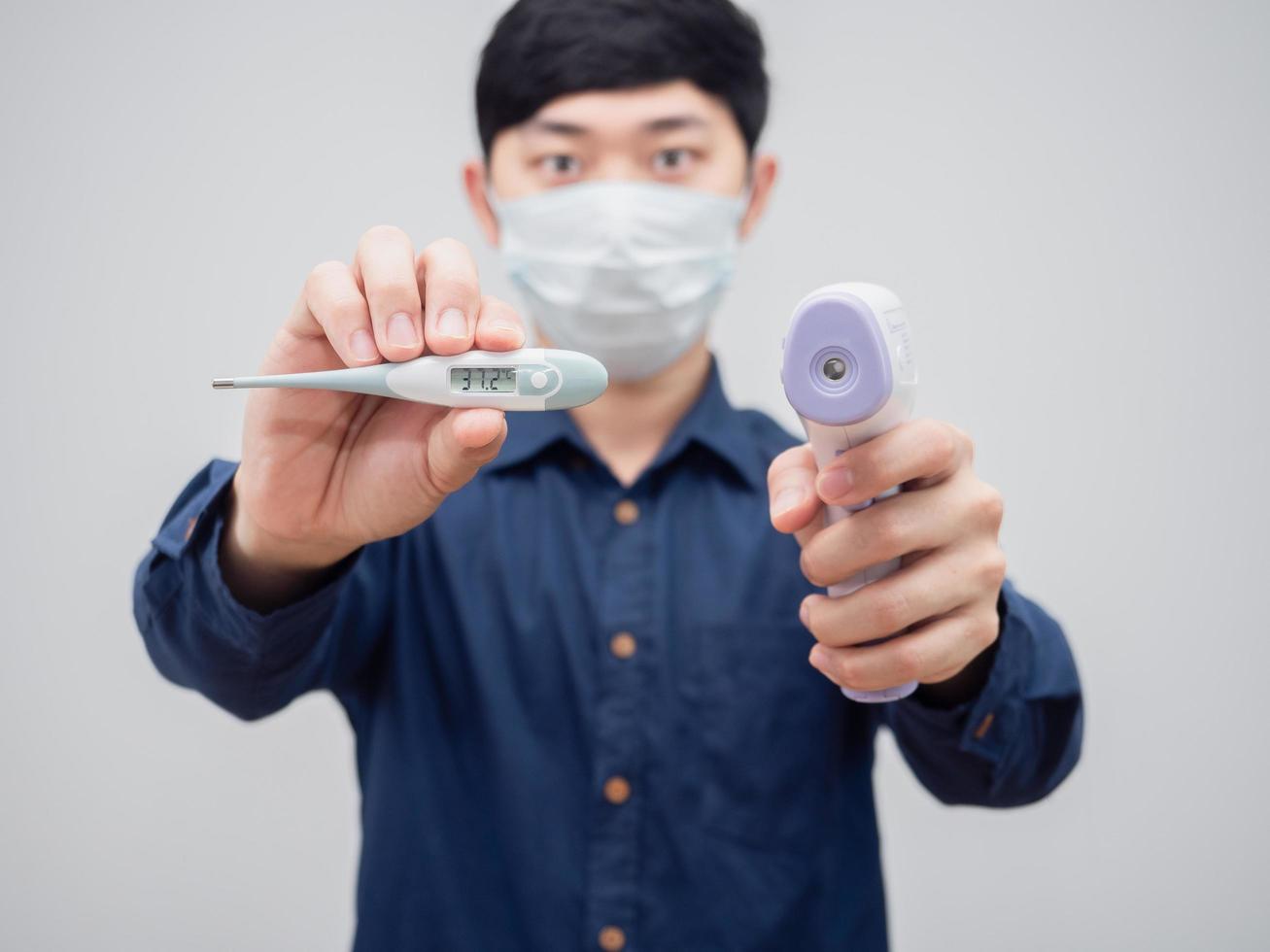 Closeup thermometer and infrared thermometer on man hand wearing mask white background photo