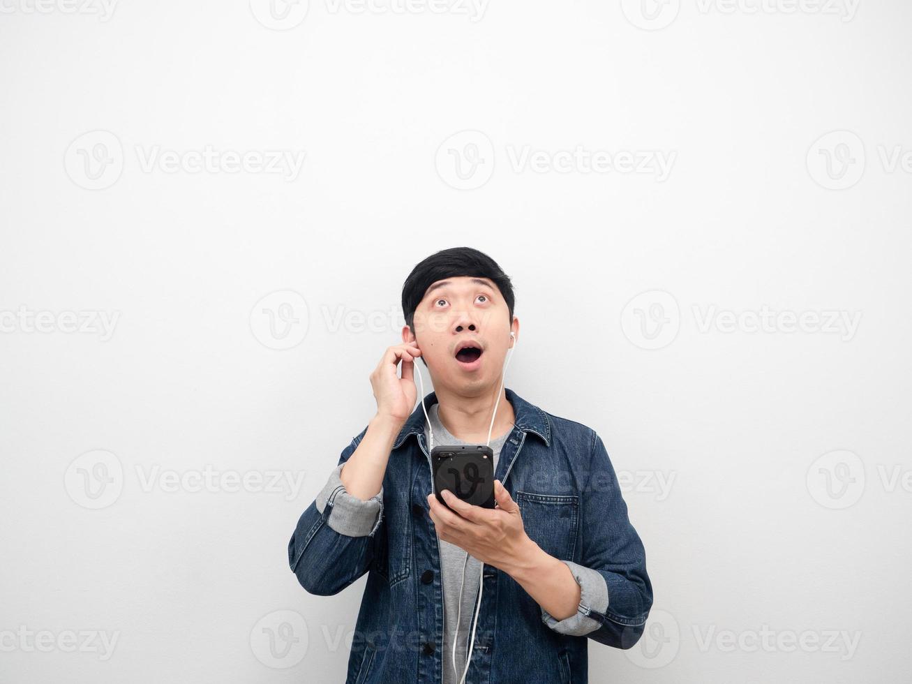 camisa de jeans de hombre usando teléfono móvil y auricular sintiendo emoción asombrada buscando espacio de copia foto