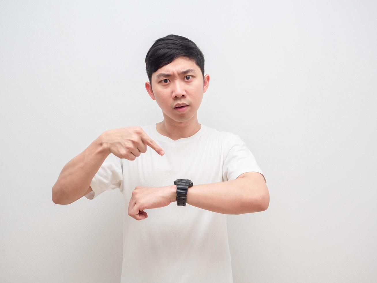 hombre asiático camisa blanca señalar con el dedo el reloj en la mano con cara seria mirar a la cámara concepto tarde y ocupado sobre fondo blanco aislado foto