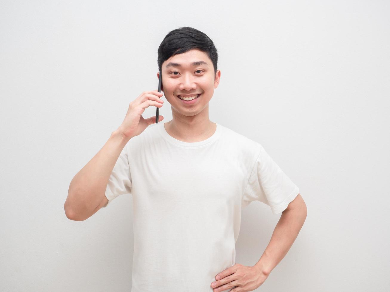 hombre asiático guapo hablando celular con una sonrisa feliz en el fondo de la pared blanca foto