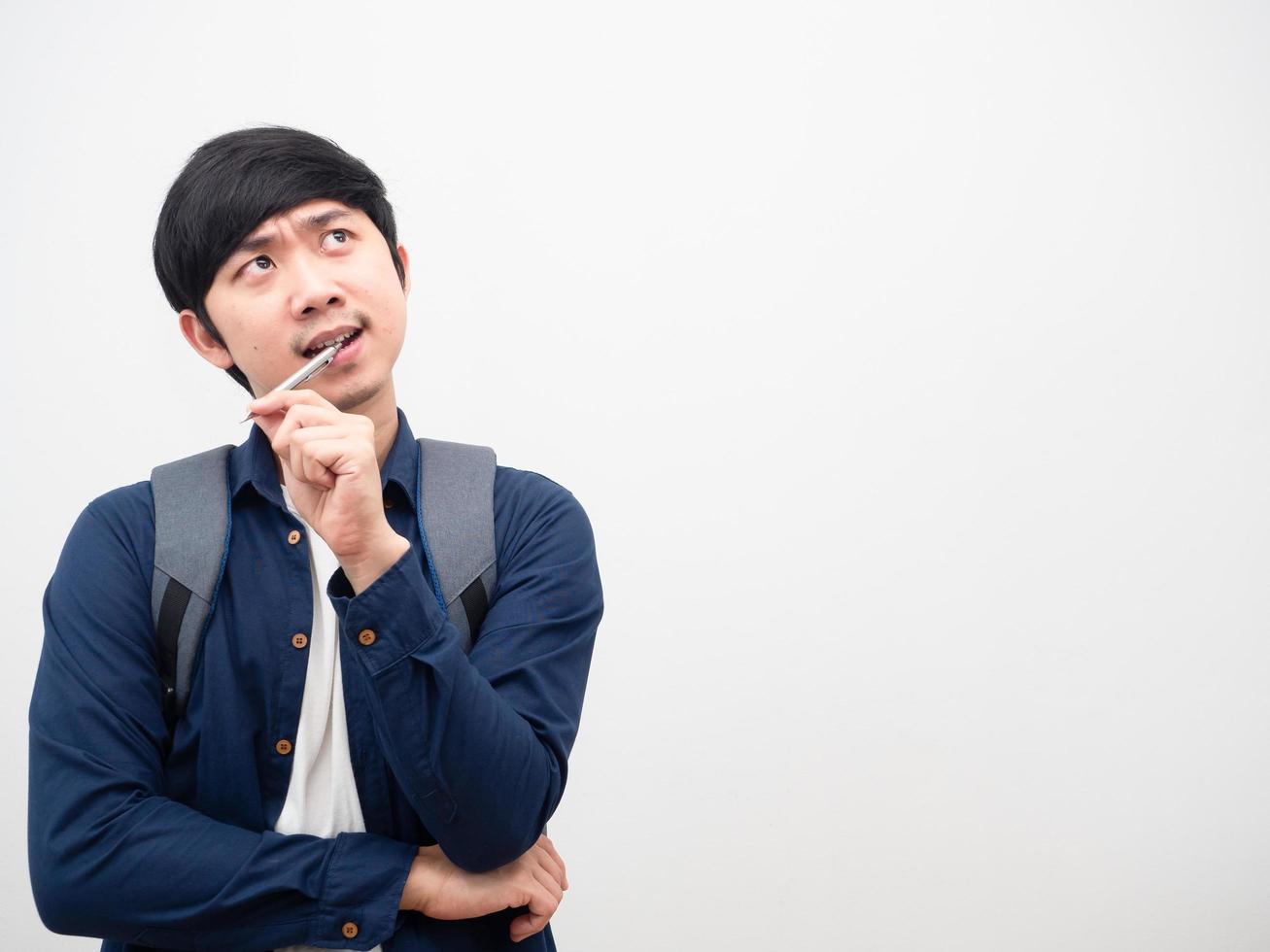 Asian man with backpack bite pen serious face thinking something look at space white background photo