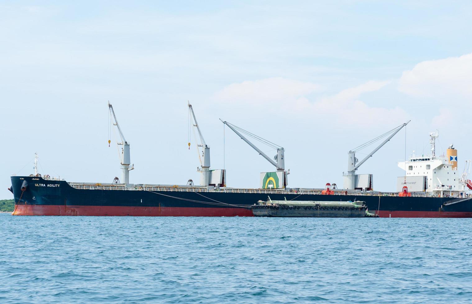 grúa en el barco industrial en el agua azul del océano y el paisaje del cielo azul, logística y concepto de barco de transporte en el mar foto