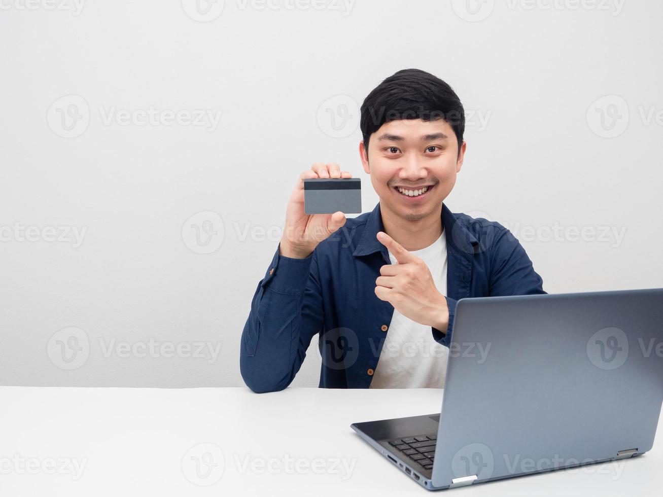 Asian man sit with laptop at the table point finger at credit card in hand photo