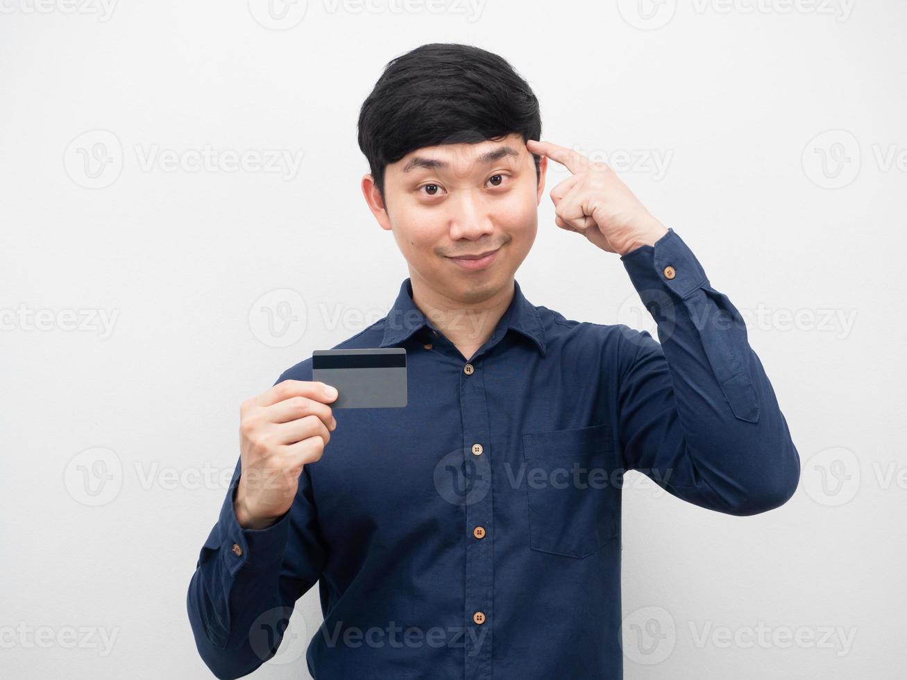 hombre asiático sonriendo sosteniendo una tarjeta de crédito y señalando con el dedo a su cabeza para pensar foto