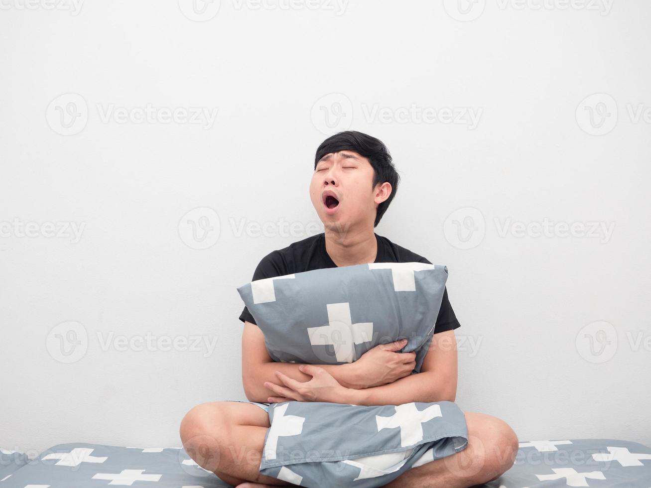 Asian man sit on the bed hug pillow feeling sleepy and yawn photo