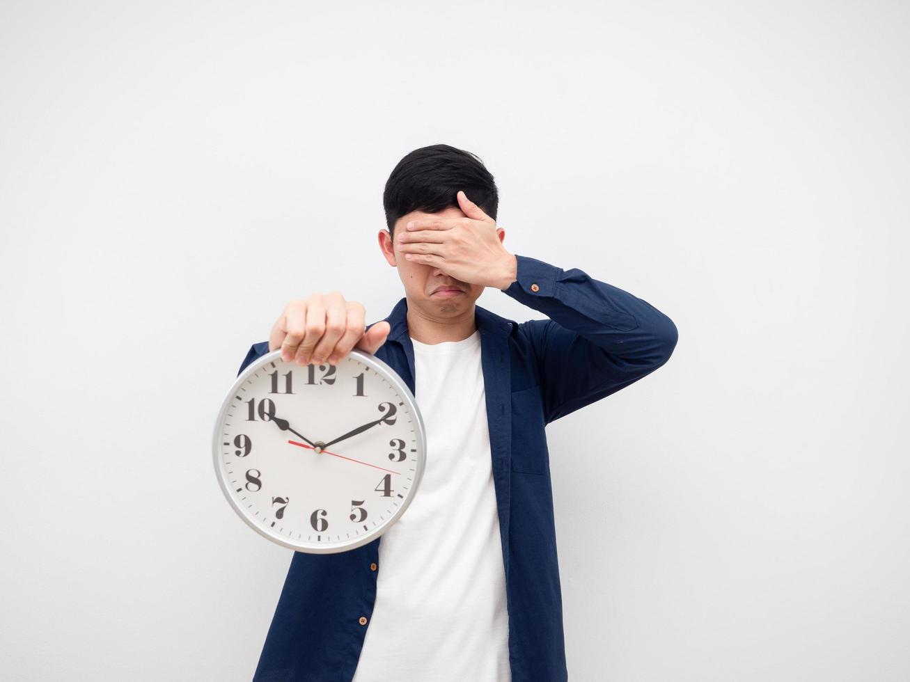 hombre asiático triste emoción cierra su cara a mano sosteniendo el reloj en la mano sobre fondo blanco, hombre trabajando tarde concepto sosteniendo el reloj 10 minutos después de las 10 am. foto