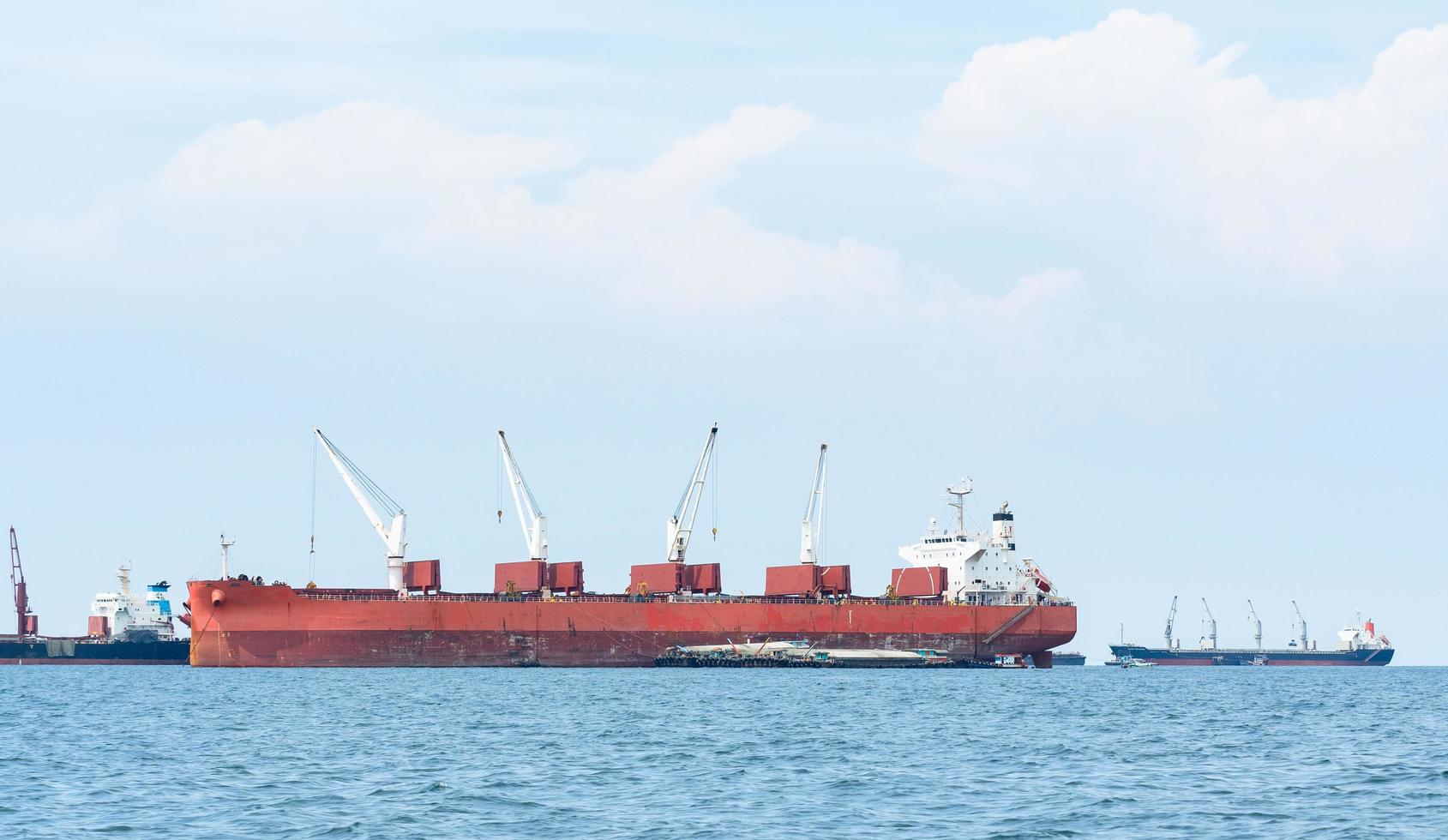 barco grande de color rojo con una gran grúa en el océano azul y el paisaje del cielo azul, barco industrial en el concepto logístico del mar foto