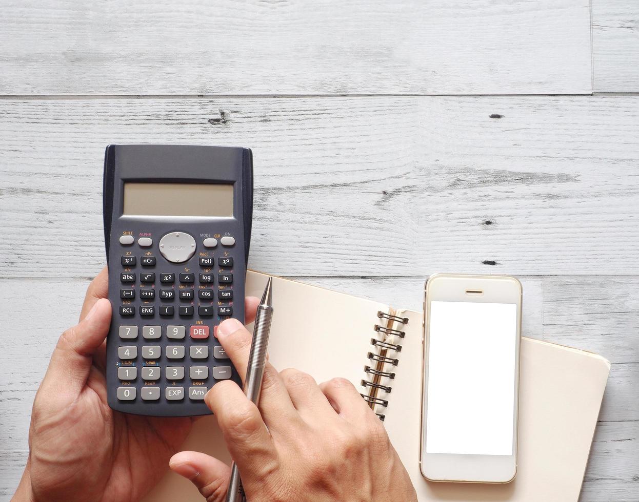 Hand with silver pen using the calculator for calculate budget with smartphone and blank page notebook on white wood background top view space business concept photo