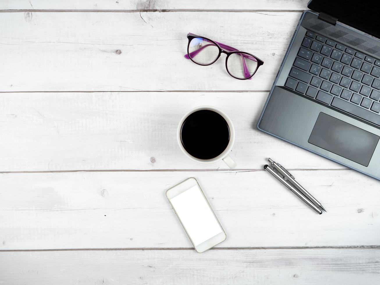 Top view workspace laptop glasses coffee cup and two silver pen with smartphone white screen copy space photo