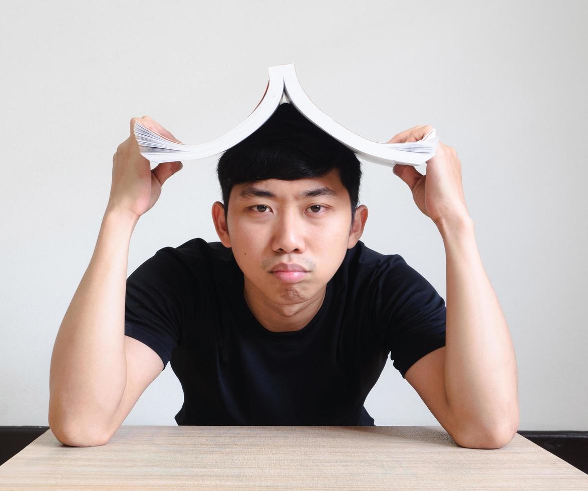 un joven aburrido y desanimado cierra el libro sobre su cabeza en blanco aislado, el estudio y el concepto de tarea foto