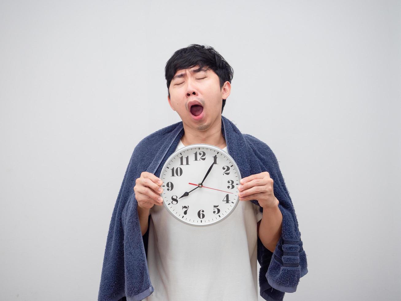 Sleepy man yawn show clock in his hand and cover body by towel on white background photo