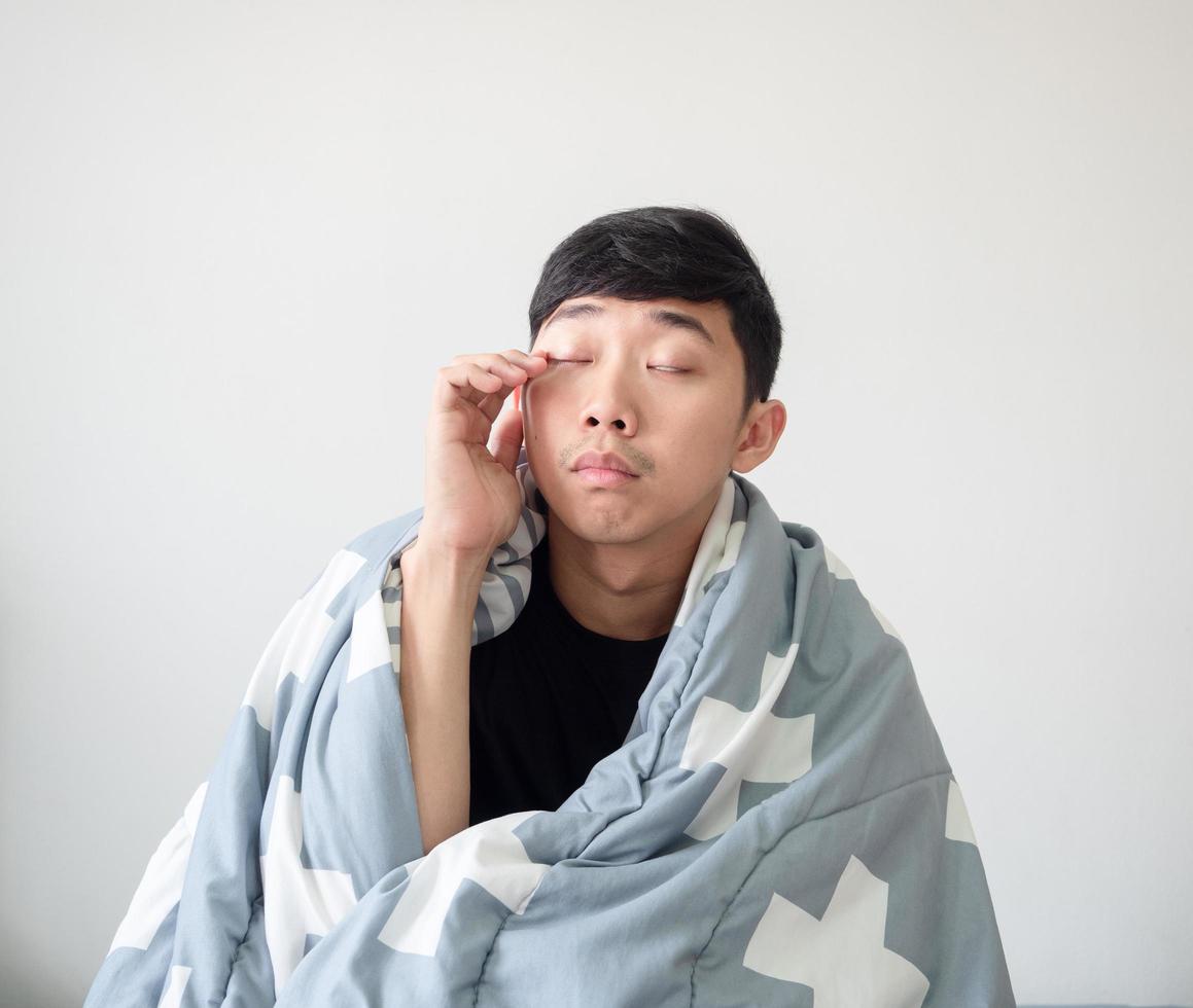 Man wake up with the blanket cover his body touch eye by hand and feel sleepy on white isolated,Sleepy man concept photo