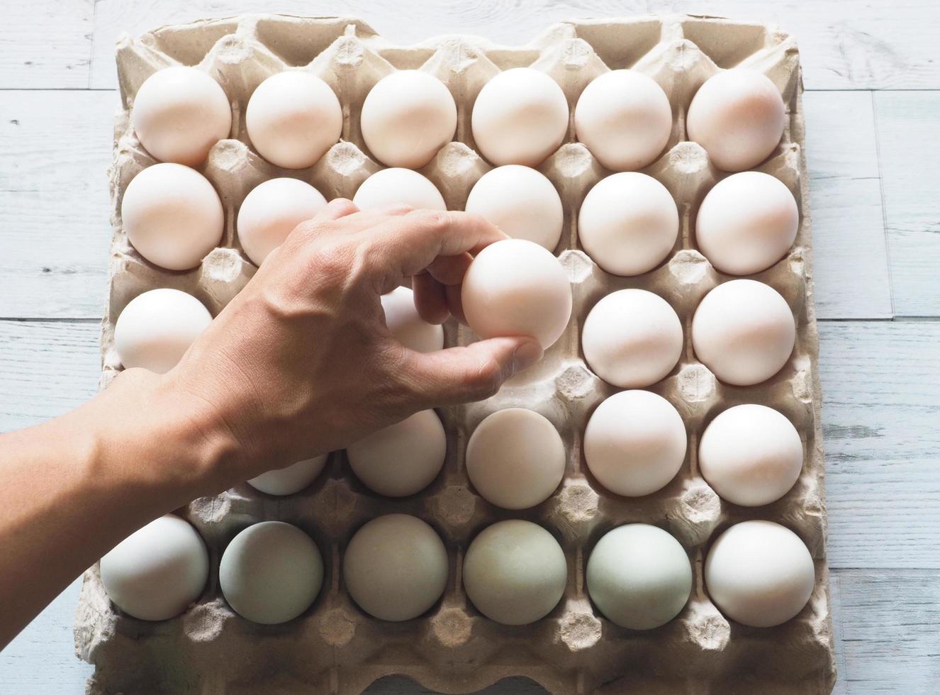 Hand holding duck eggs on group duck eggs in carton box on white wood table with nature shadow and light photo