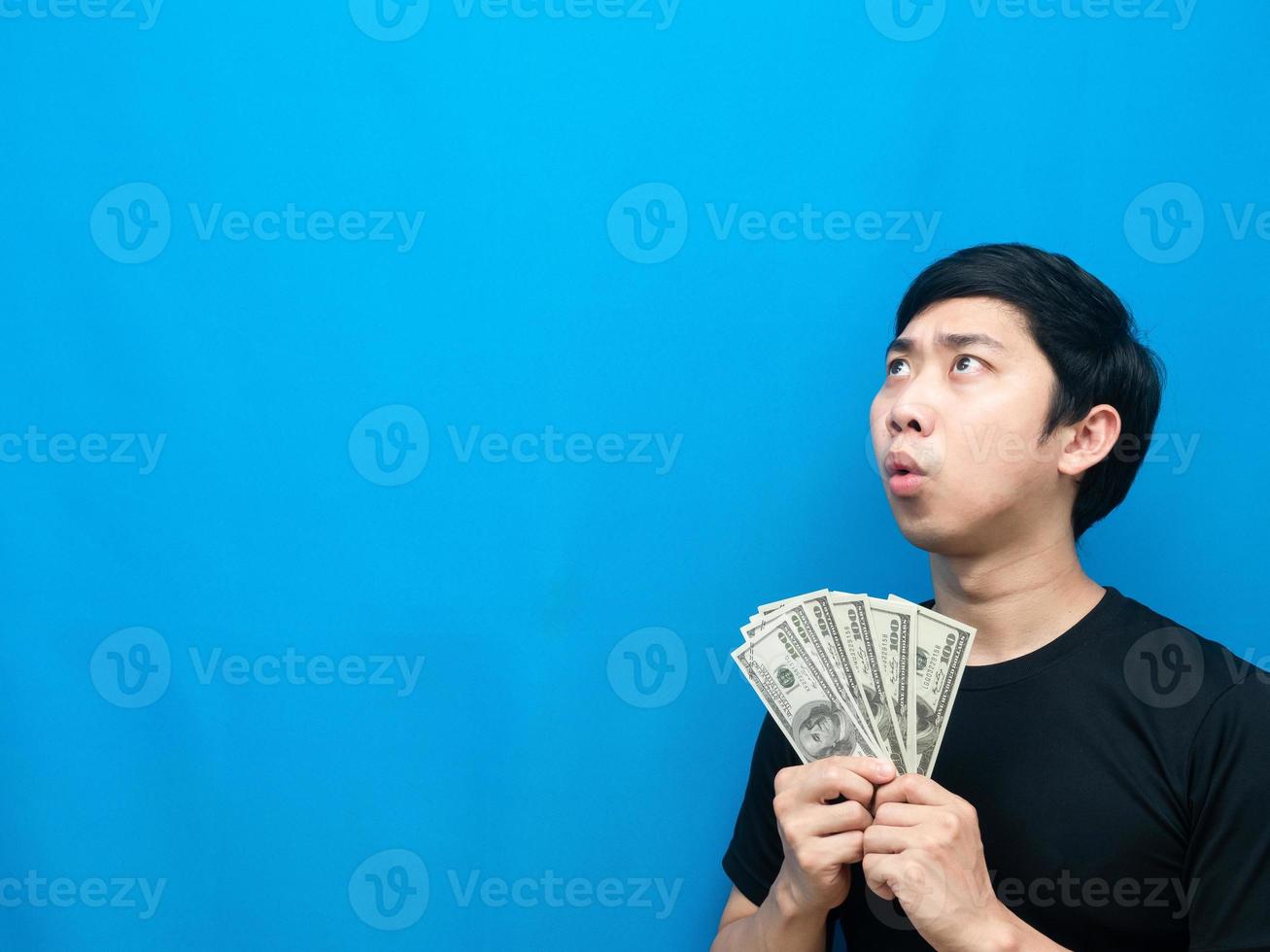 Man holding money feeling amazed looking at copy space blue background photo