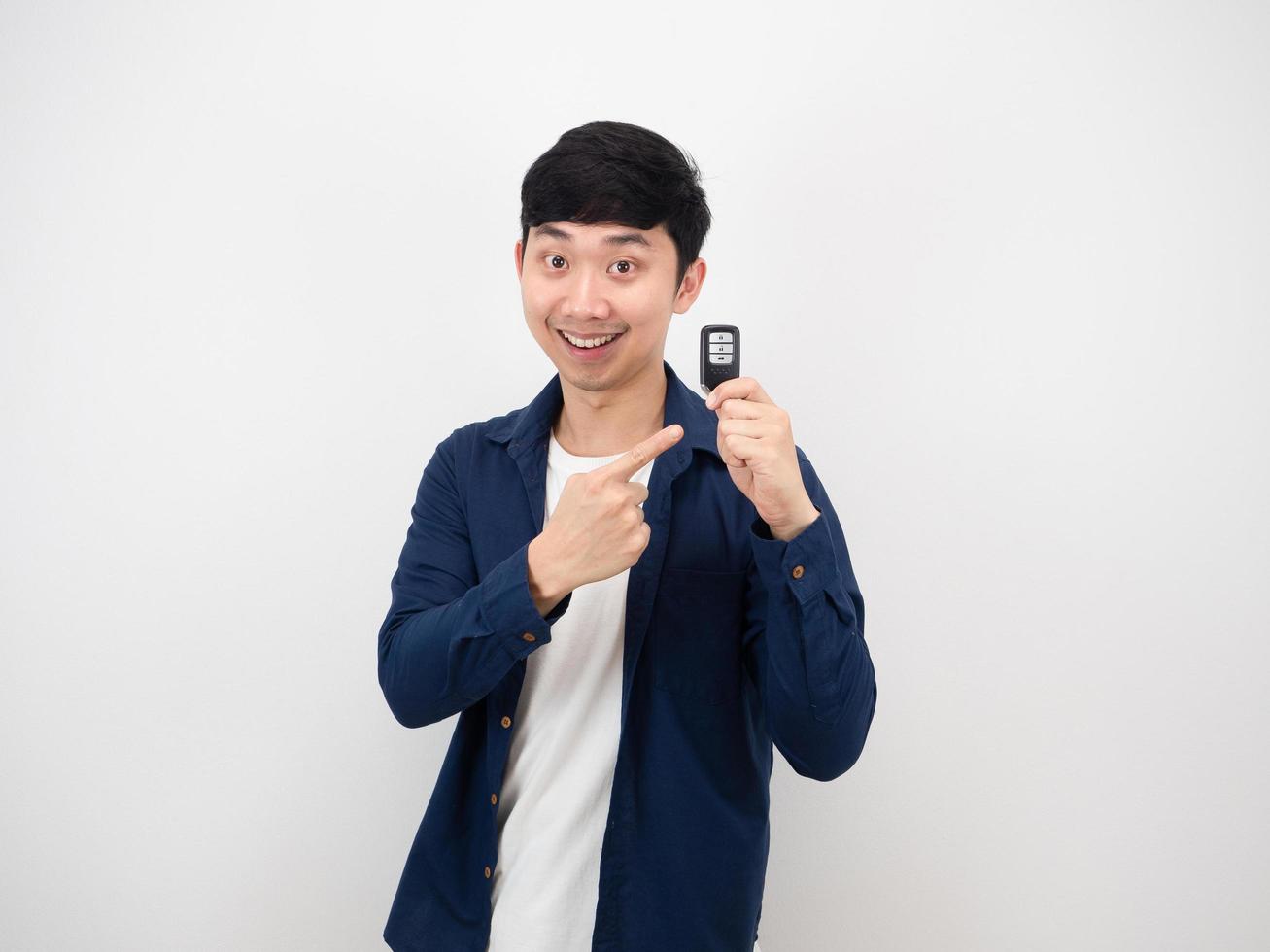 Handsome asian man point at car key in his hand with happy smile cheerful on white wall background photo