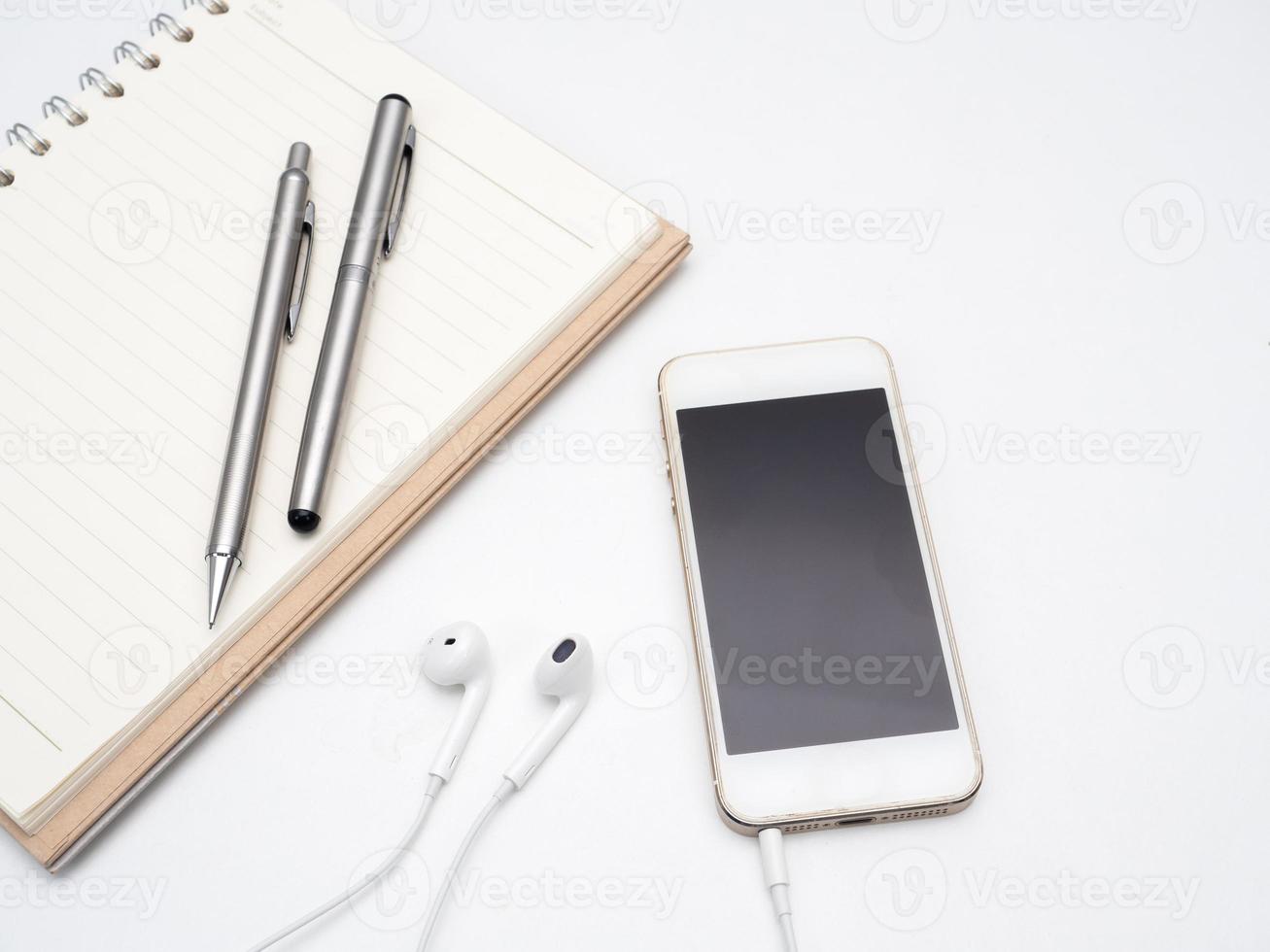 Close up mobile phone with ear phone and pen with diary book on table photo