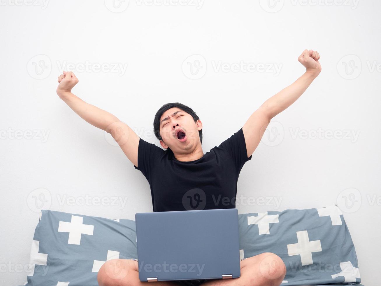 Man with laptop sitting on the bed feeling sleepy photo