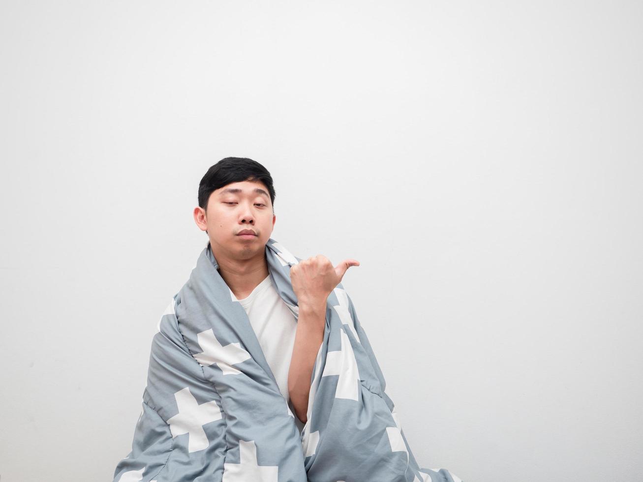 Asian man cover body by blanket and bored face point finger right side copy space on white background,Don't want to wake up concept photo