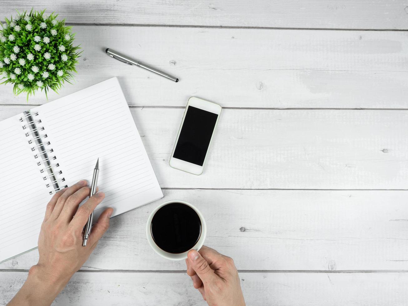 Workspace on white wood desk top view copy space,Notebook blank page with hand hold silver pen and coffee cup photo