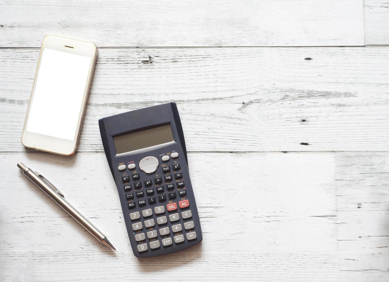 Smartphone white screen and silver pen and calculator on white wood table top view copy space sunlight shadow business concept photo