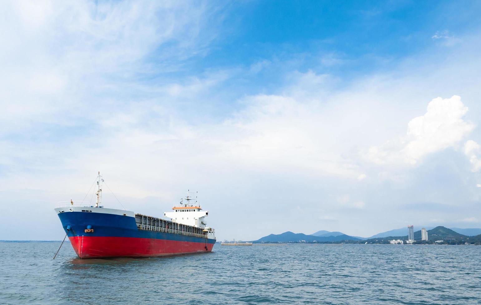 Cargo ship red blue color in the ocean and island mountain background with the blue sky and cloudy landscape photo