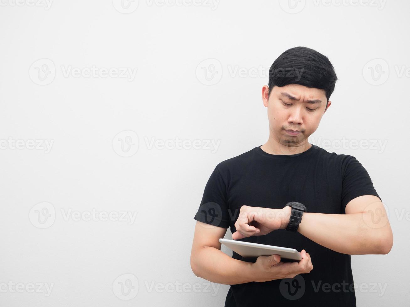 Asian man holding tablet and looking at his watch copy space photo