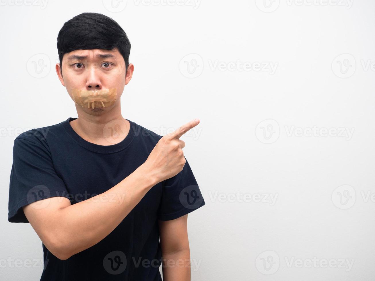 hombre camisa negra cinta cerrar la boca sentir miedo señalar con el dedo el espacio de la copia foto