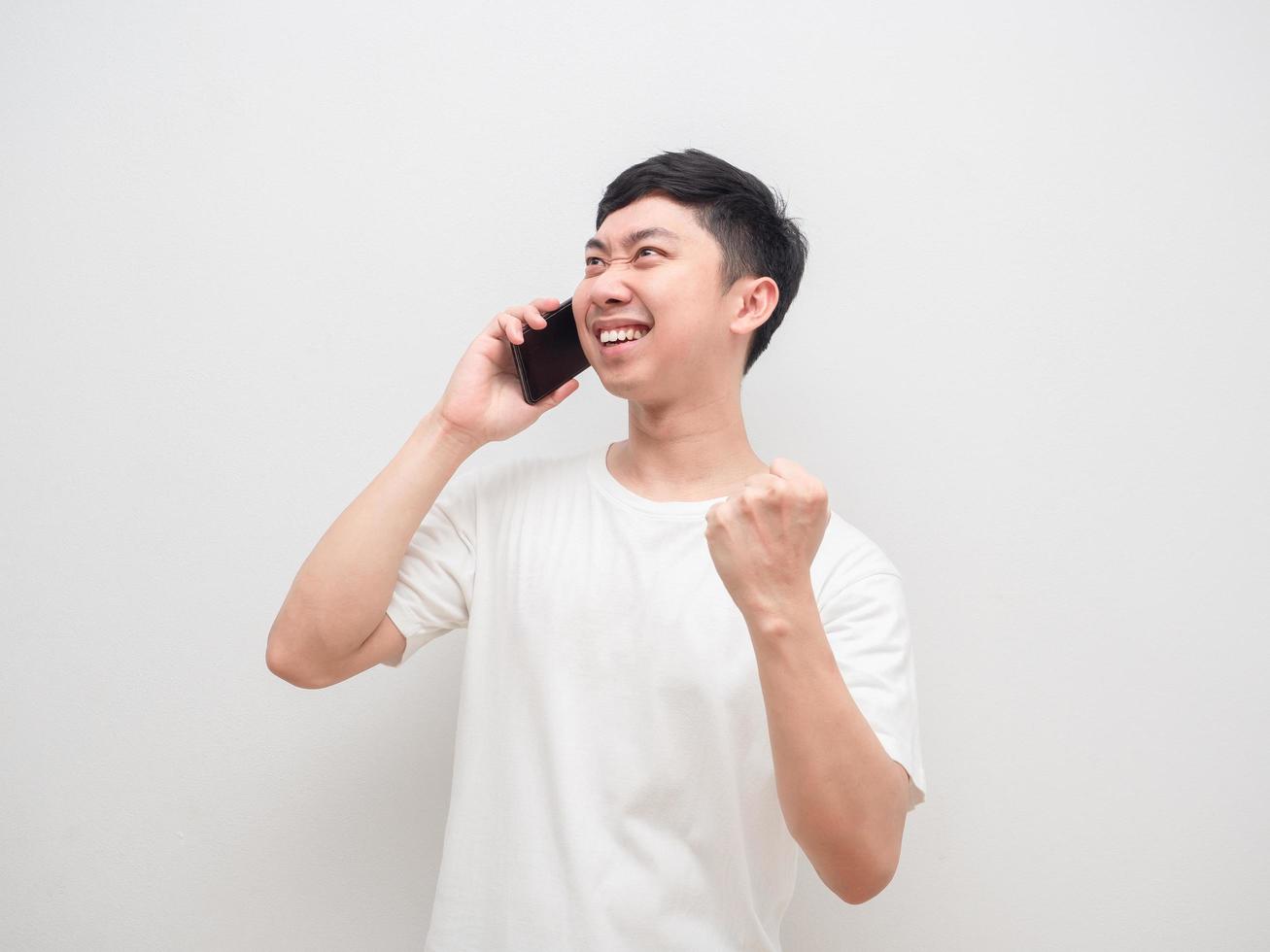 el hombre hablando con el teléfono celular muestra el puño hacia arriba sintiéndose feliz con fondo blanco foto