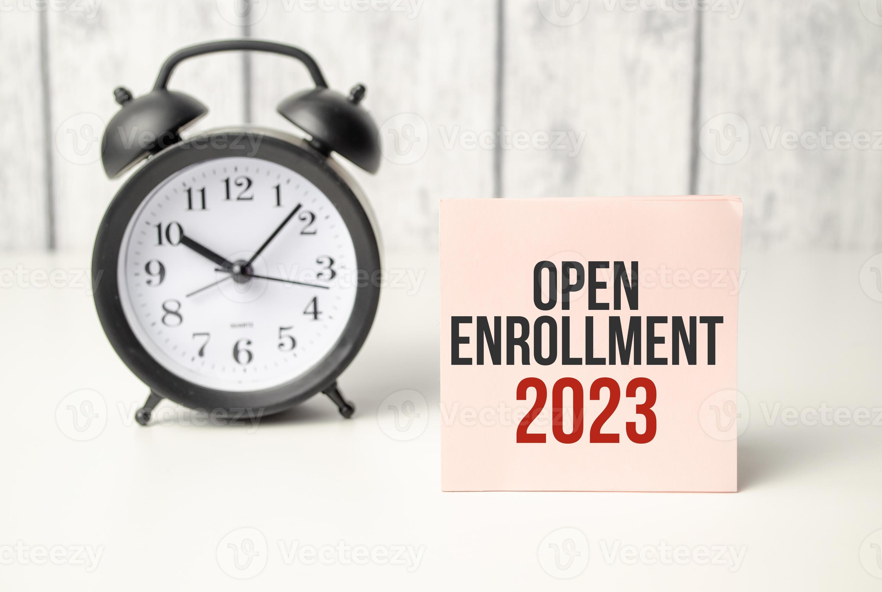 The word OPEN ENROLLMENT 2023 written on pink sticker and alarm clock
