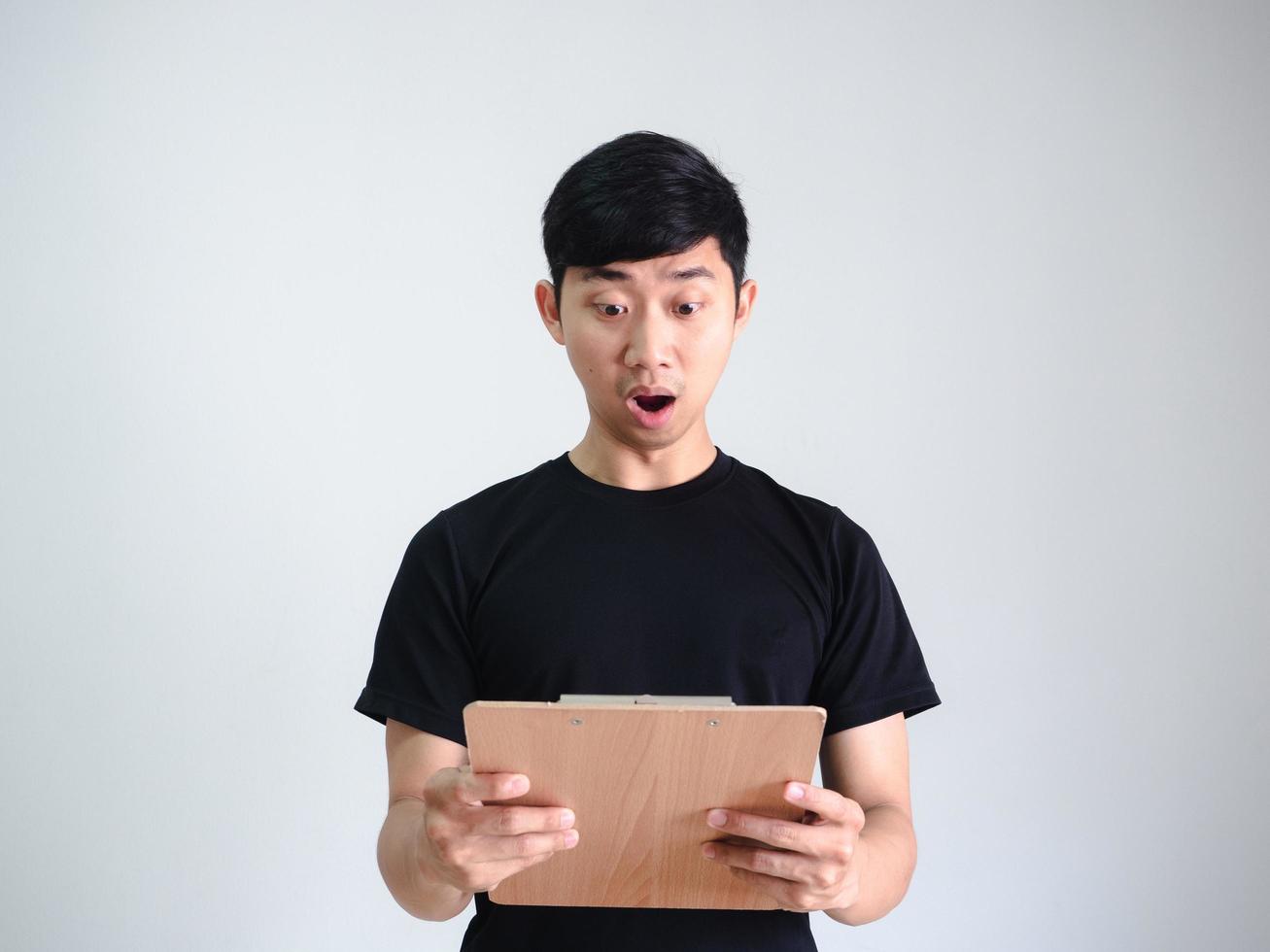 Asian man black shirt shocked face and looking at wood clipboard in hand on white isolated,Business concept photo