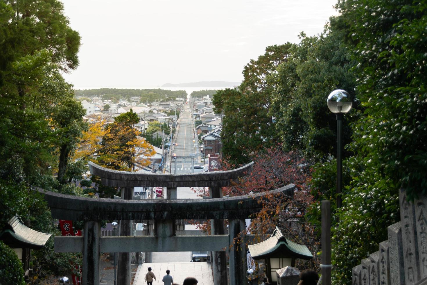 view of torii stone entrance gate on mountain hill of Miyajidake Shrine temple in sunset daytime with local street walking street leads into sea shore photo