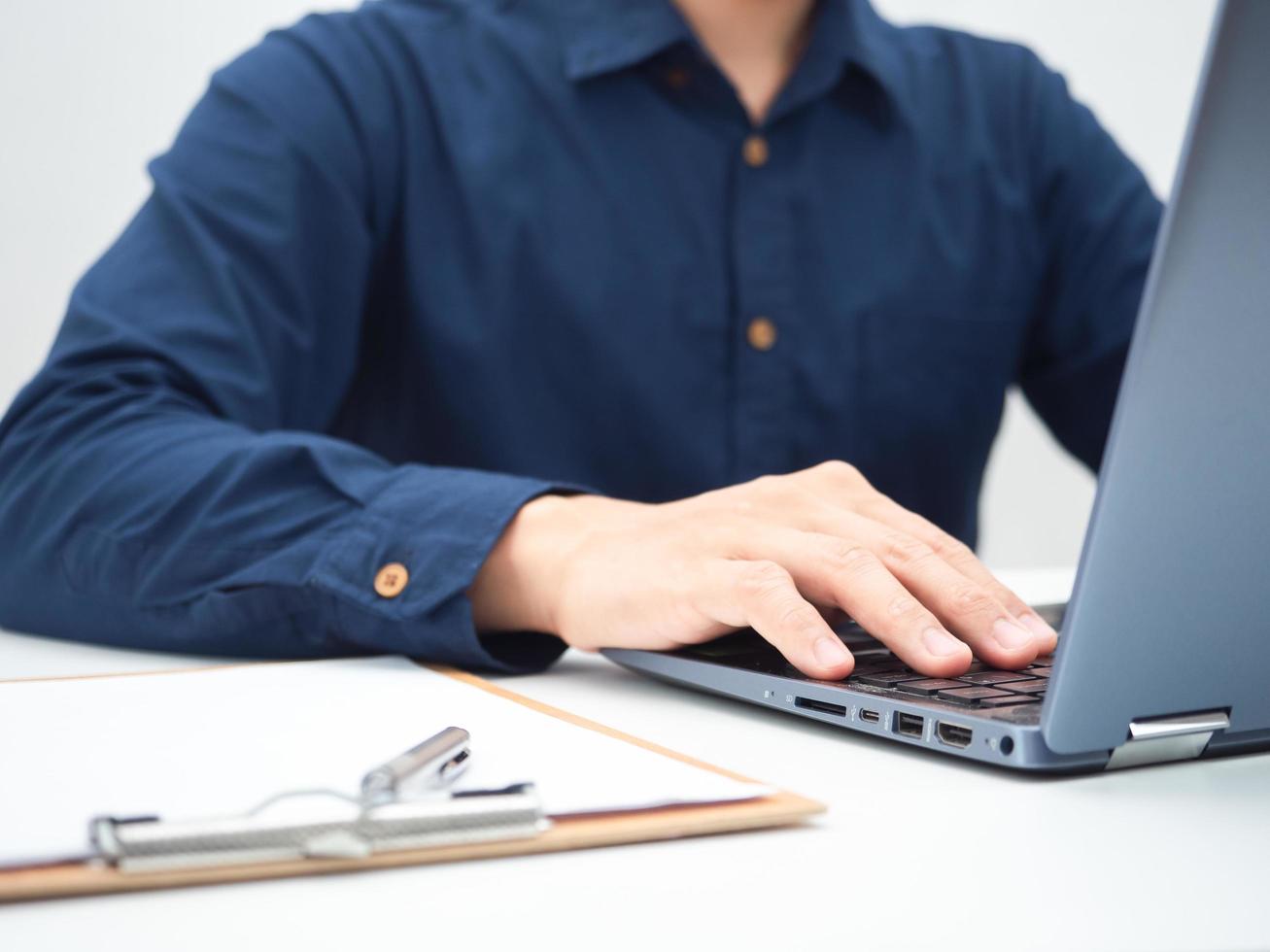 Crop shot of man using laptop on the table with document board and pen photo