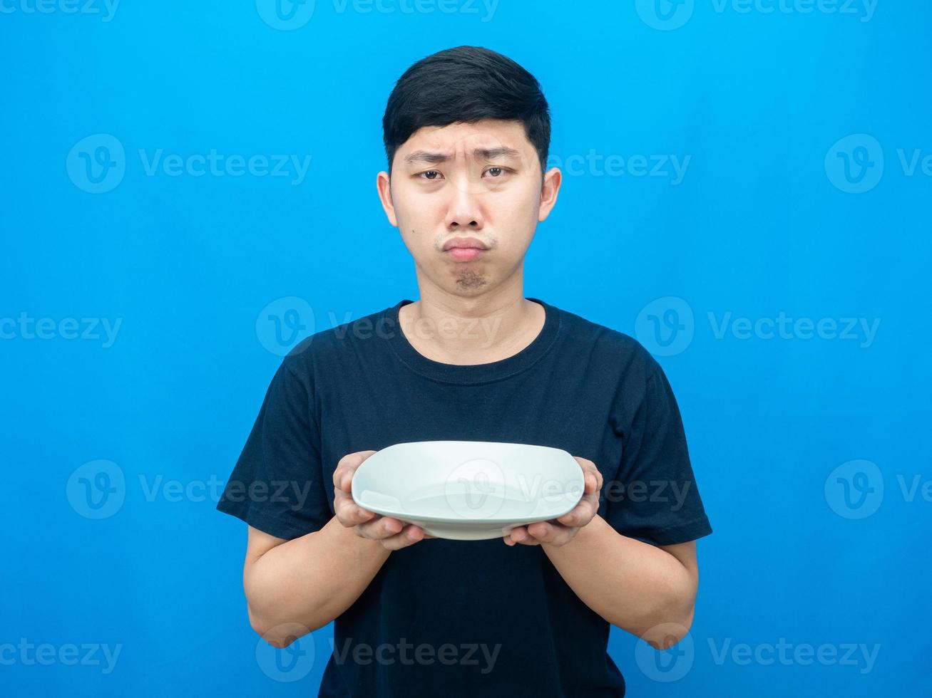 hombre hambriento con gesto de plato vacío quiere comida fondo azul foto