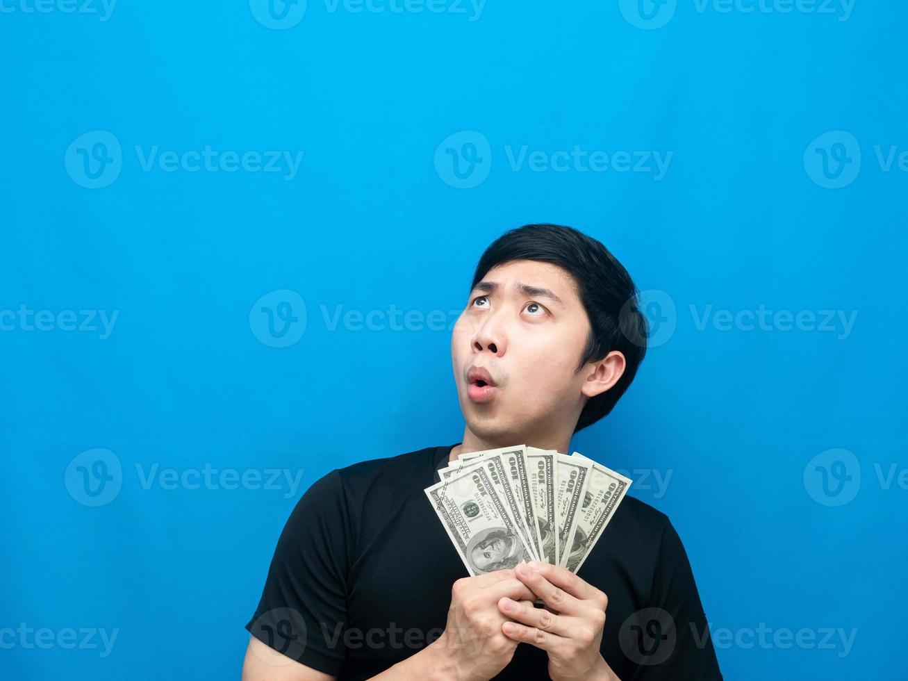 Man holding money feeling amazed looking up at copy space blue background photo