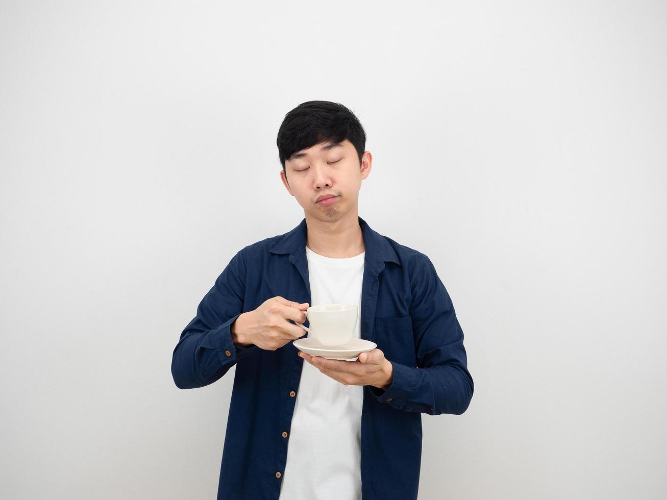 hombre asiático sosteniendo una taza de café sintiéndose somnoliento cierra su ojo sobre el concepto perezoso de fondo blanco foto