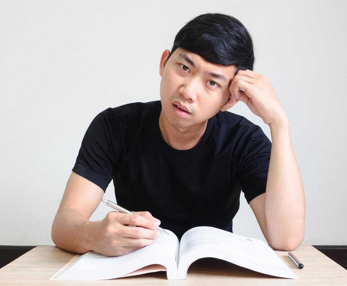 Young man strain and bored face with read the book on the desk on white isolated,Homework concept photo